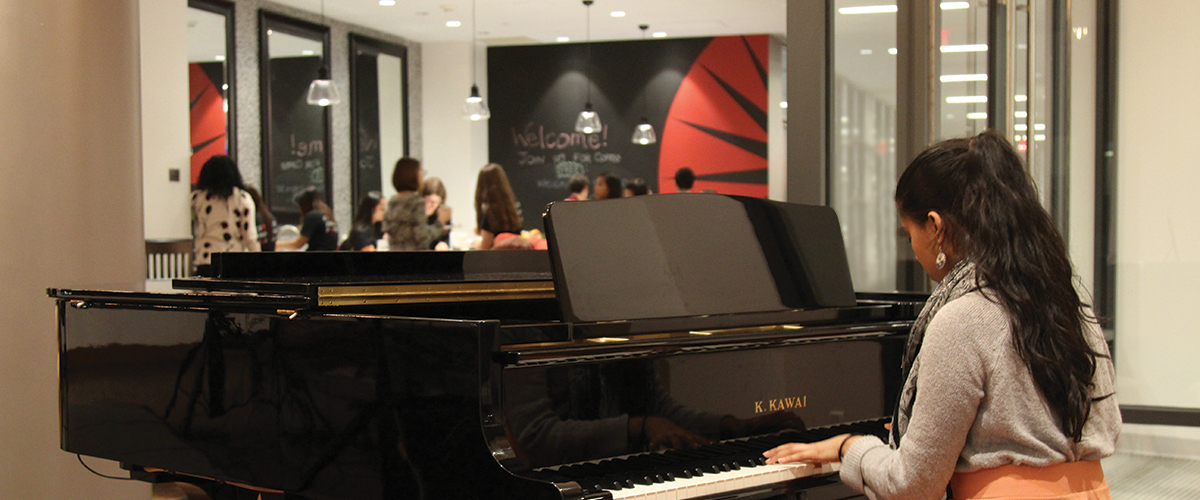 Student playing piano in the Fireside Lounge and other students hanging out around the coffee bar area