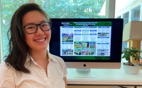 Student standing next to her computer monitor showing her research poster